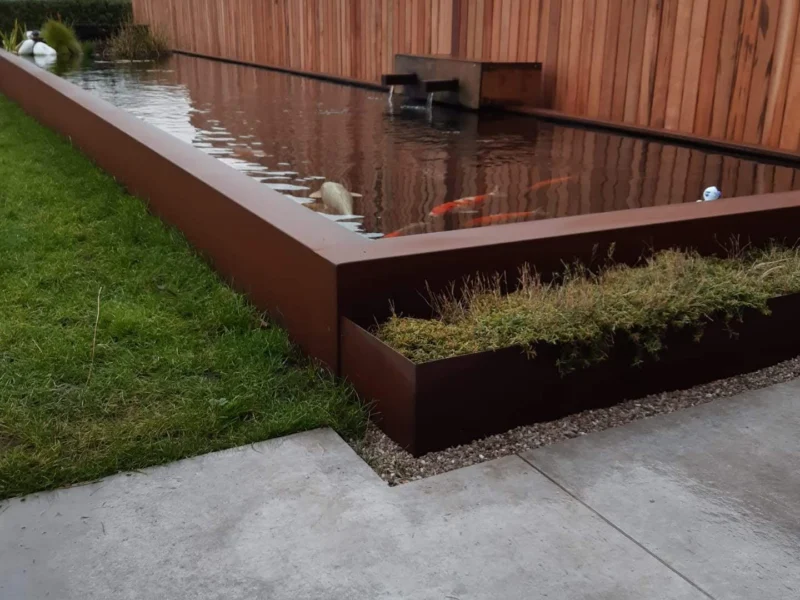 Verhoogde vijverrand en borders in cortenstaal met waterval langs een houten tuinscherm