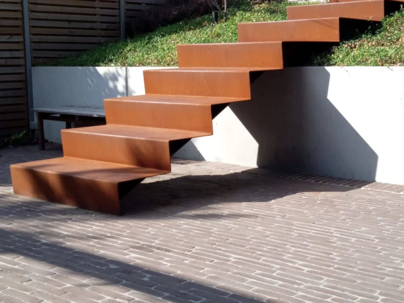 Zwevende tuintrap in cortenstaal langs een betonnen keerwand