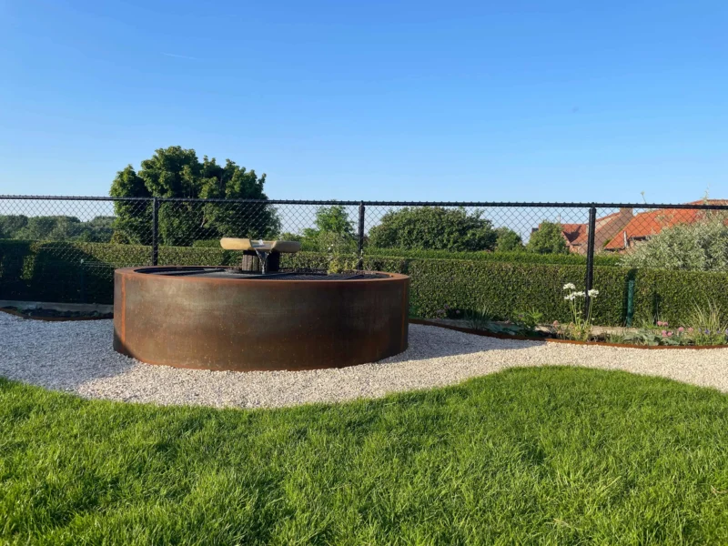 Ronde vijver in cortenstaal in een grindbed, omringd door gazon, in een tuin in Elsegem