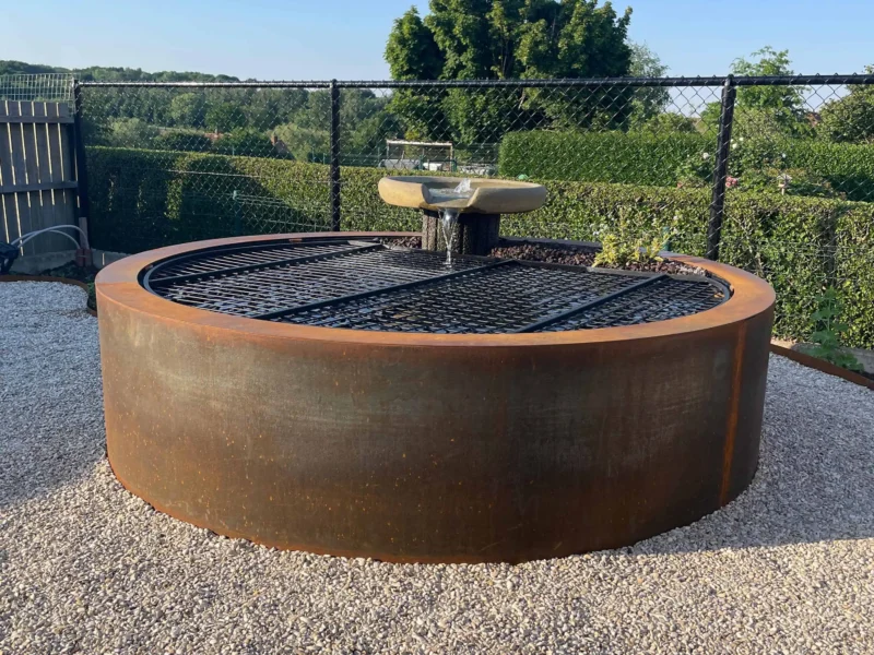 Ronde vijver in cortenstaal met waterornament en beplanting op de rand