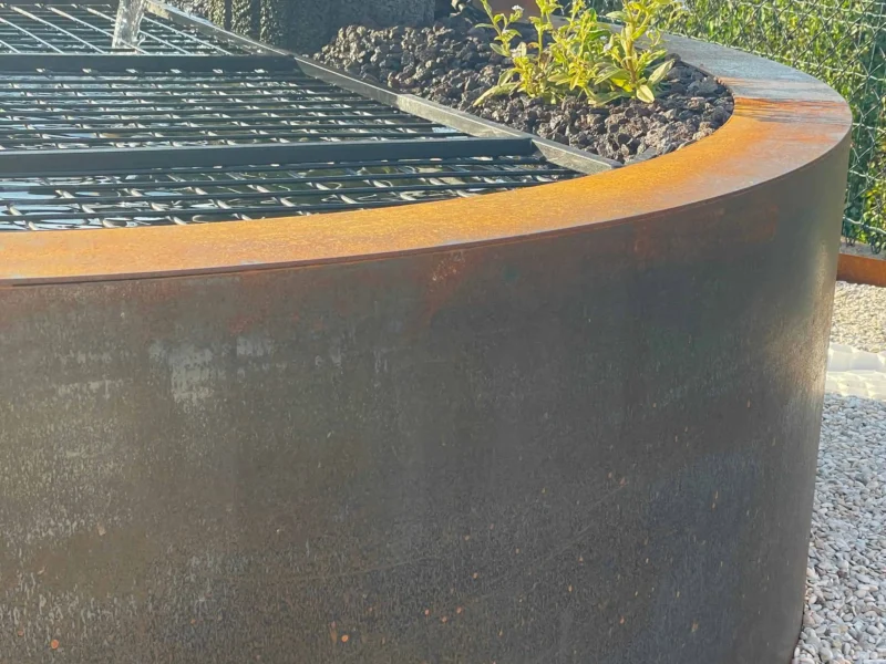 Detail van de vijverrand in cortenstaal met waterval uit de stenen schaal