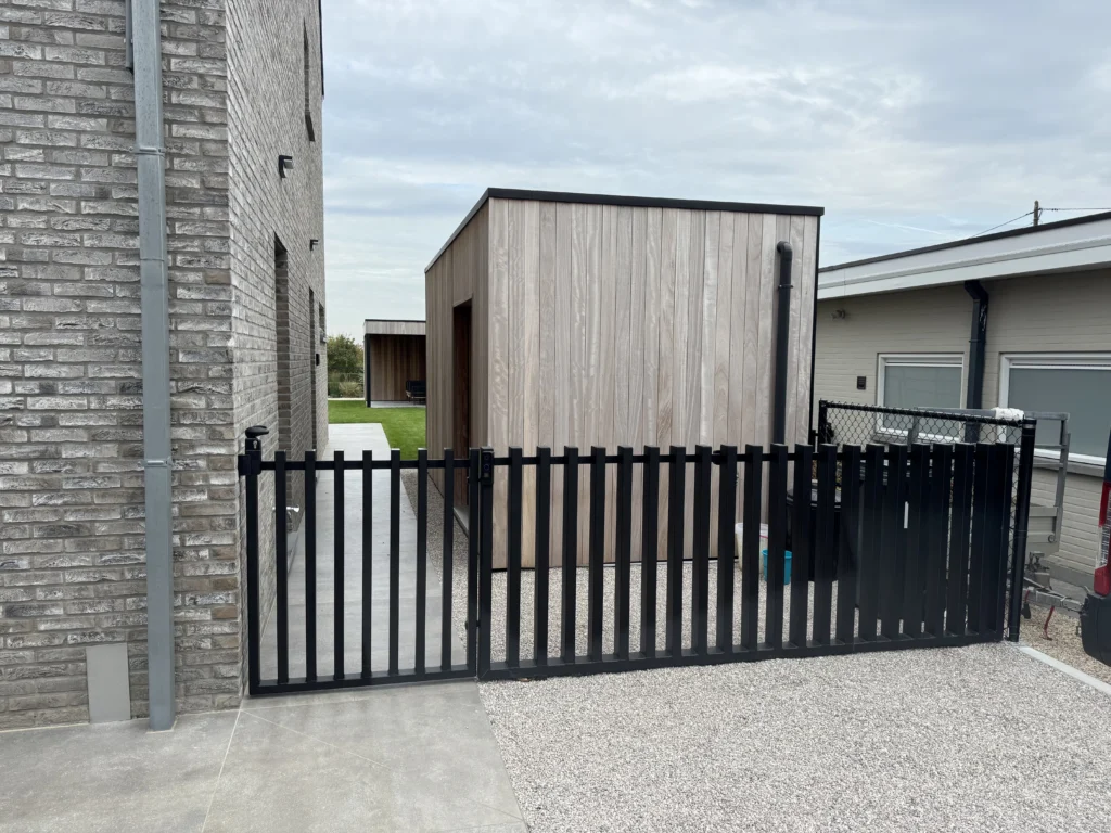 Zwart gelakte spijlenpoort met vast stuk aan een oprit