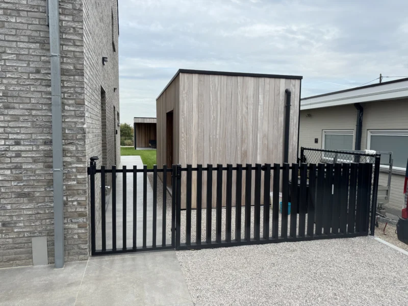 Zwart gelakte spijlenpoort met vast stuk aan een oprit